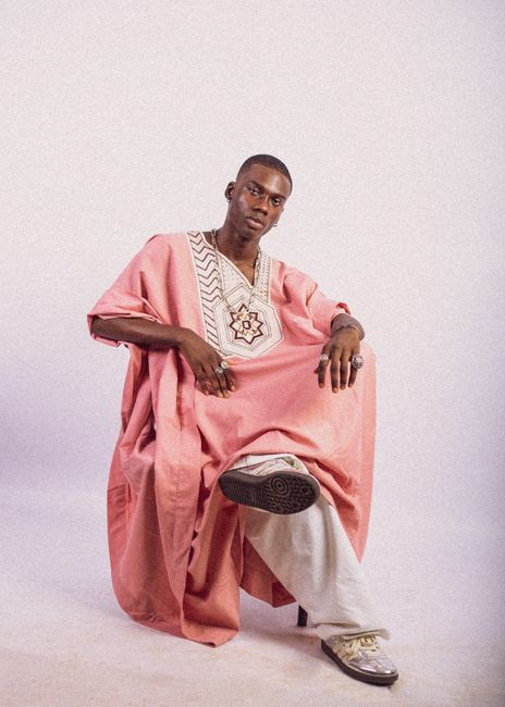 Stylish portrait of a man in pink traditional clothing on a neutral backdrop.