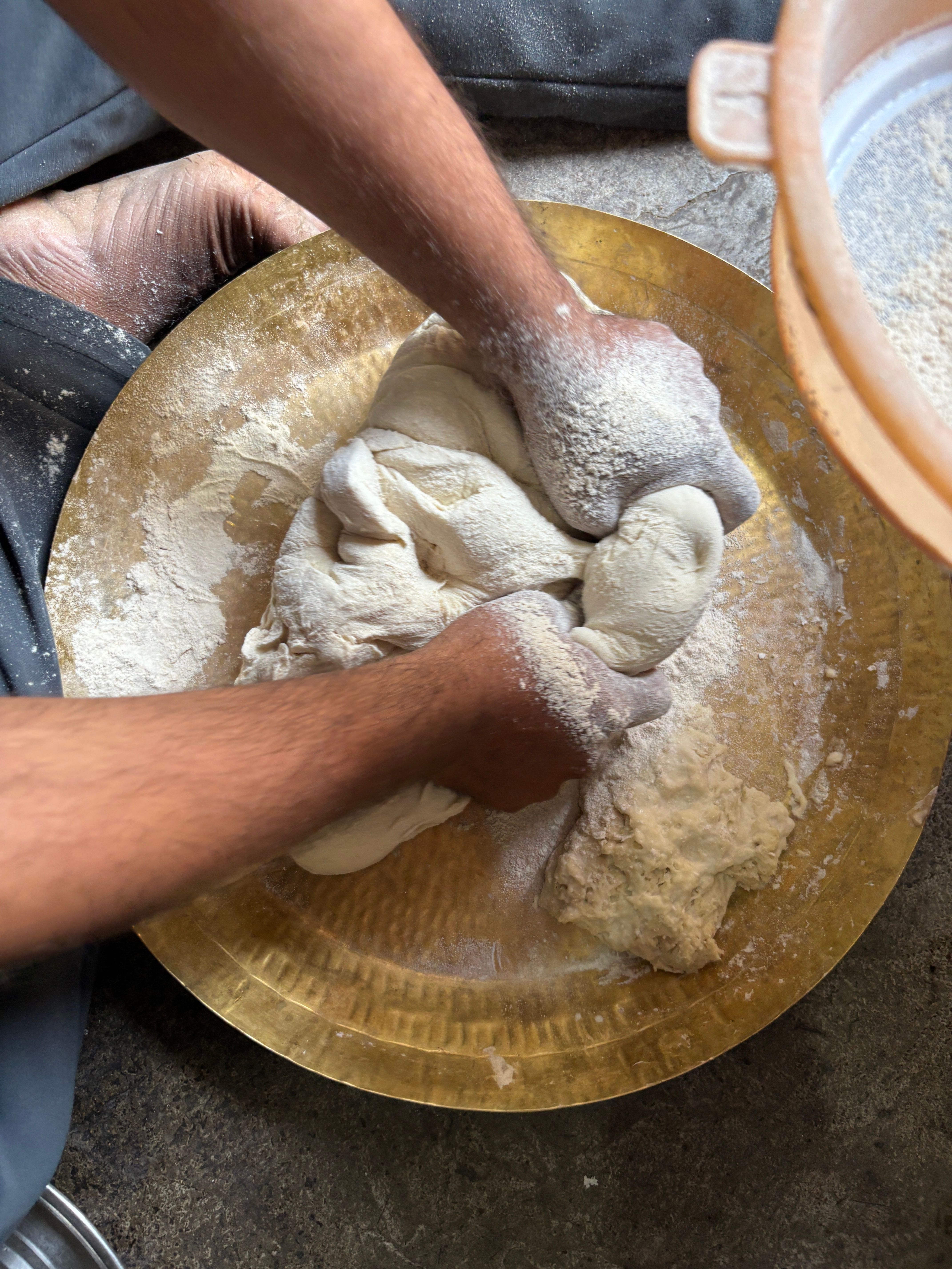 Hands kneading dough on a flour-dusted golden plate, preparing homemade bread.
