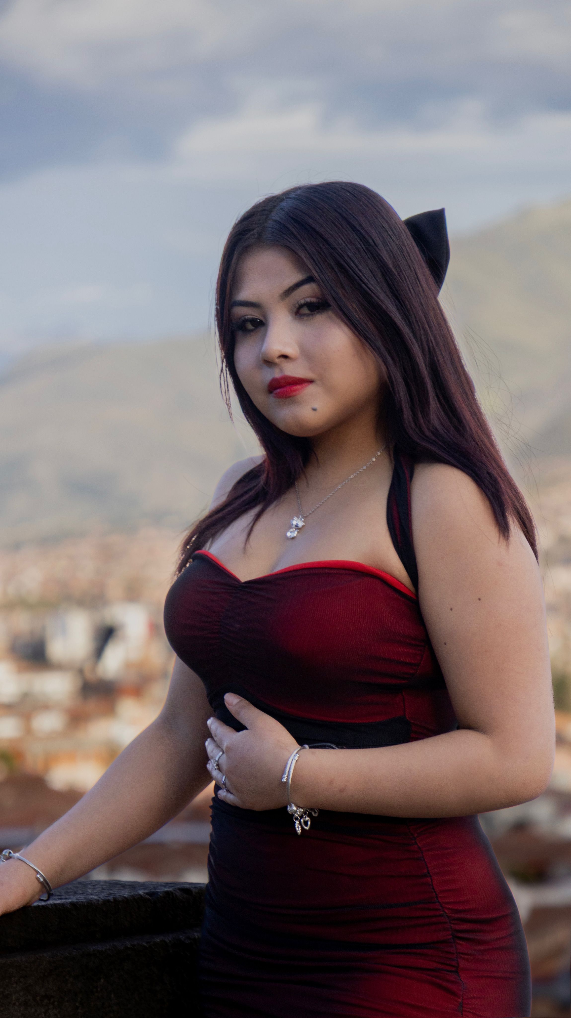 Young woman in red dress posing outdoors with Cusco's scenic backdrop.