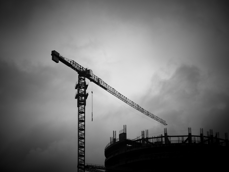 Dramatic black and white photo of a construction crane against a moody sky.