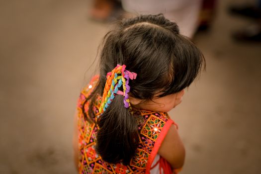 A young girl with vibrant hair accessories and traditional attire viewed from behind.