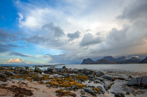 Free Dramatic coastal scene capturing rocky shores, mountains, and a vibrant sky. Stock Photo
