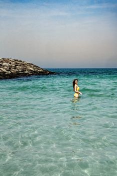 A woman in a yellow bikini swims in the clear turquoise waters of a tropical beach.