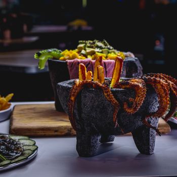 Close-up of gourmet octopus dish presented in traditional stone mortar for a unique dining experience.