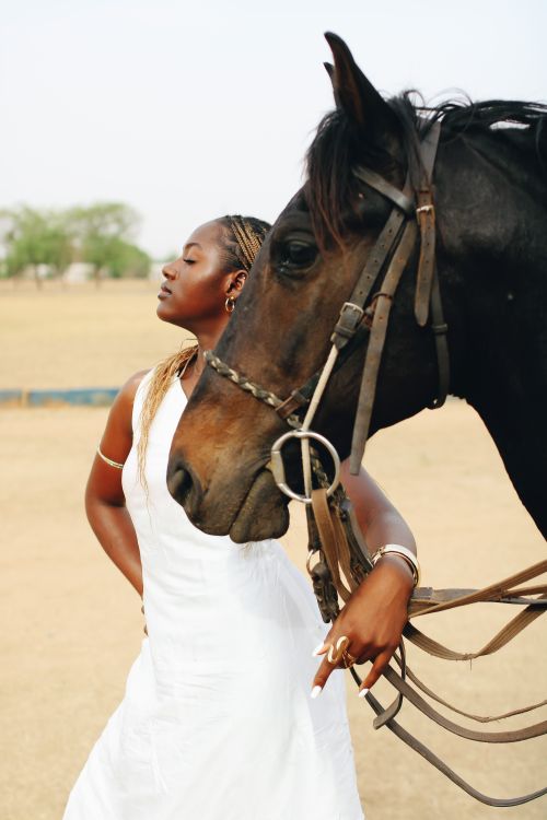 Free A stylish woman in white poses confidently with a horse in an open field setting. Stock Photo