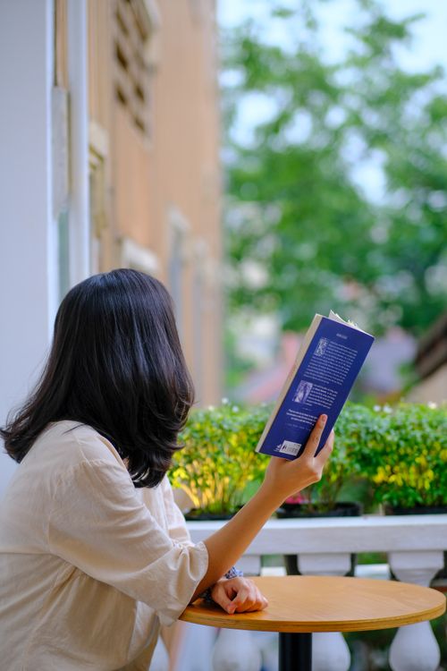 Free Young woman reading on a balcony in Hue, Vietnam reflecting a serene and relaxed moment. Stock Photo