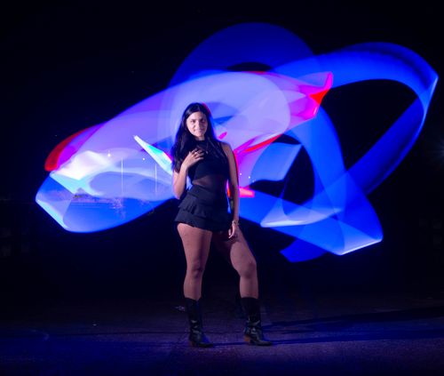 Free A woman poses with colorful light trails in the background, creating a vibrant and dynamic night scene. Stock Photo
