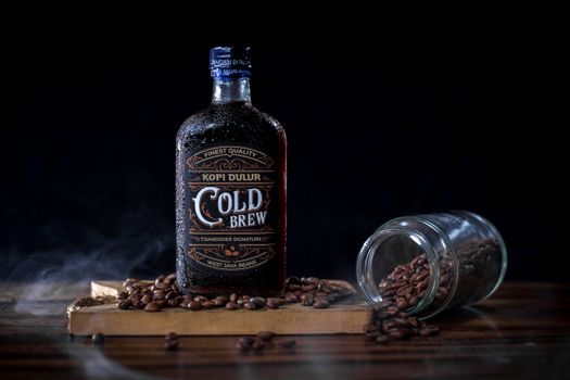 A cold brew coffee bottle with West Java beans, surrounded by scattered coffee beans.