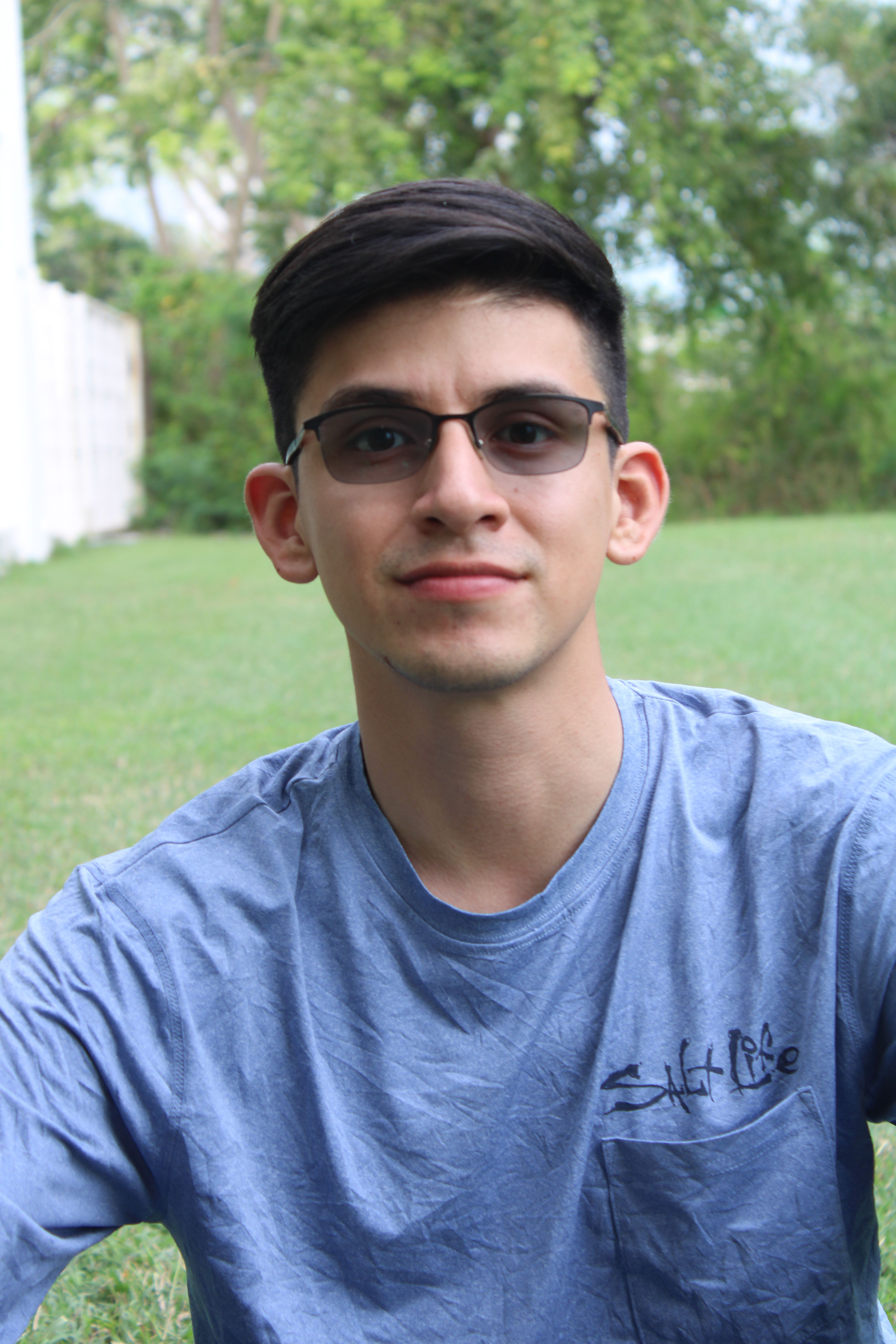 Portrait of a young man wearing glasses, seated on grass in Chetumal, Mexico.