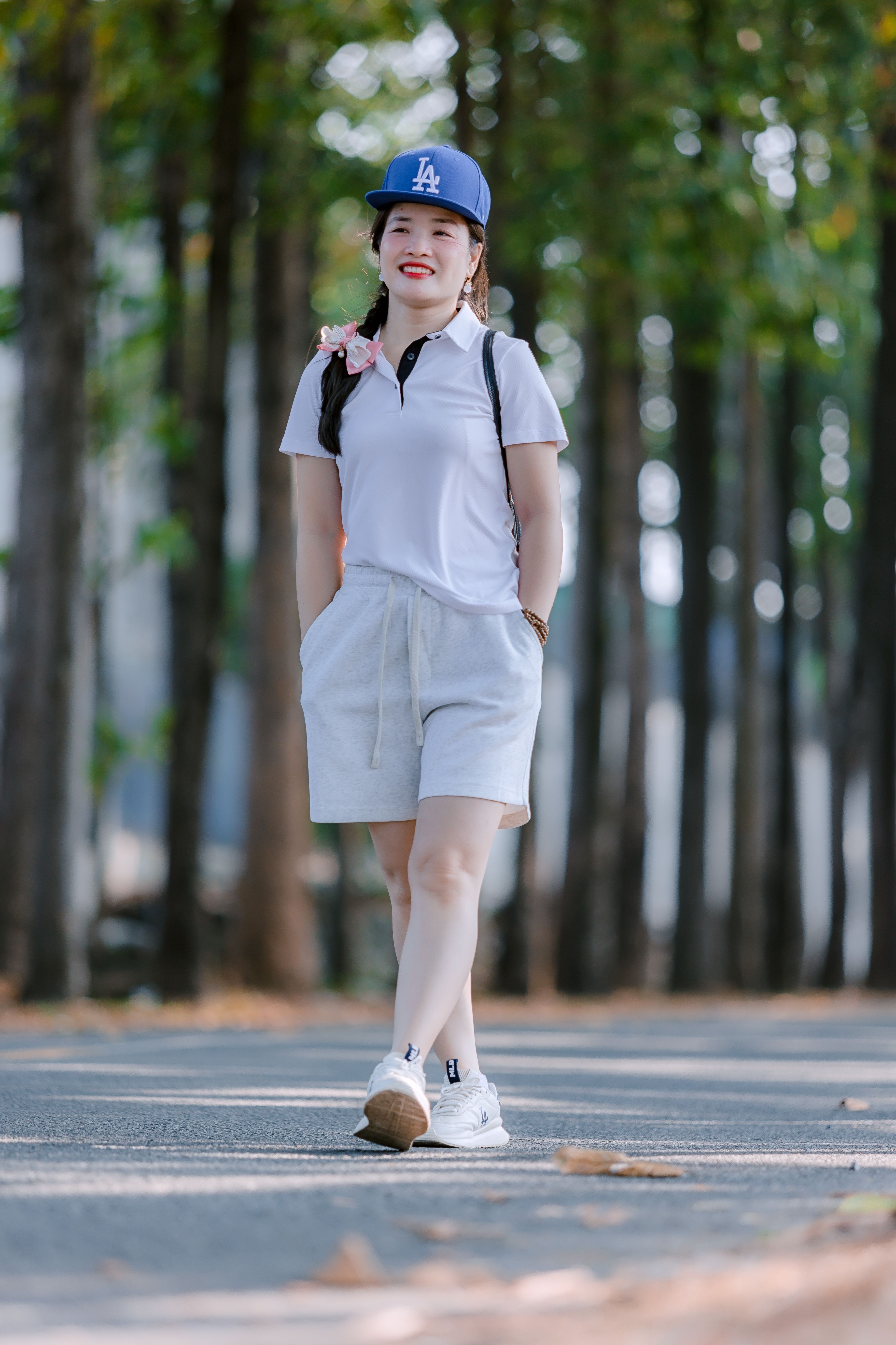 A smiling young woman strolls confidently in a sunlit park lined with trees.