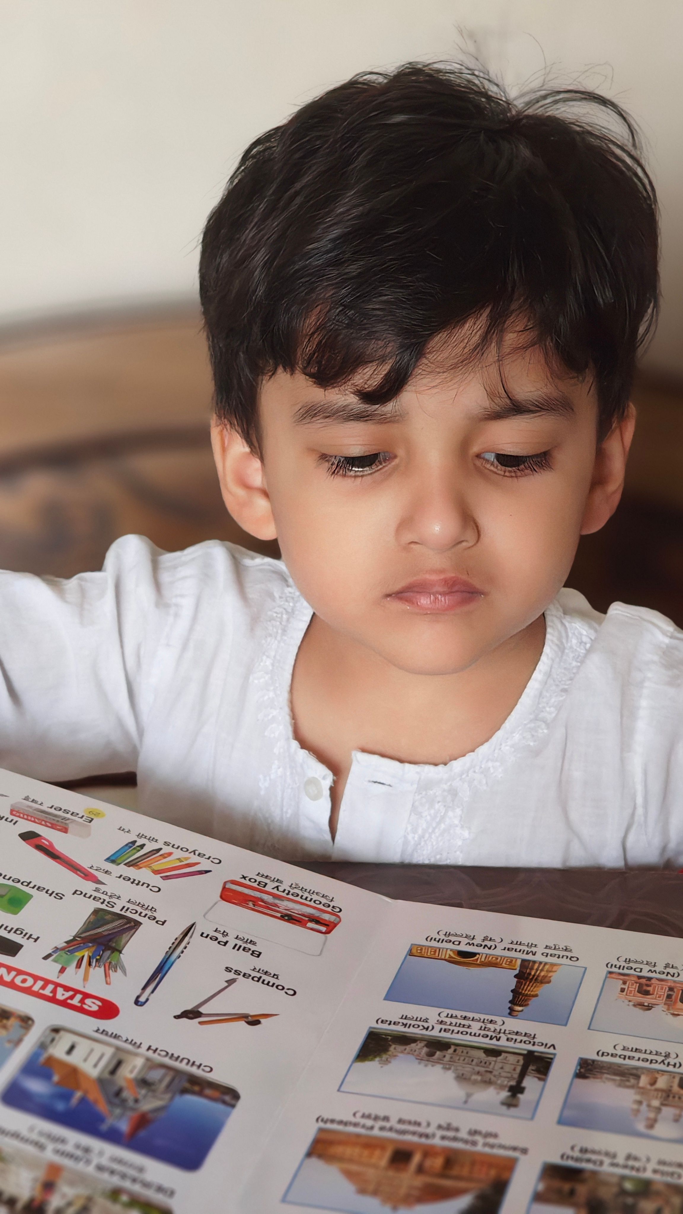 Young child attentively reading a colorful educational book indoors, focused on learning.