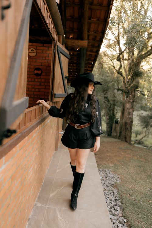 Free Stylish woman wearing a black western hat and boots, posing outside a rustic building. Stock Photo