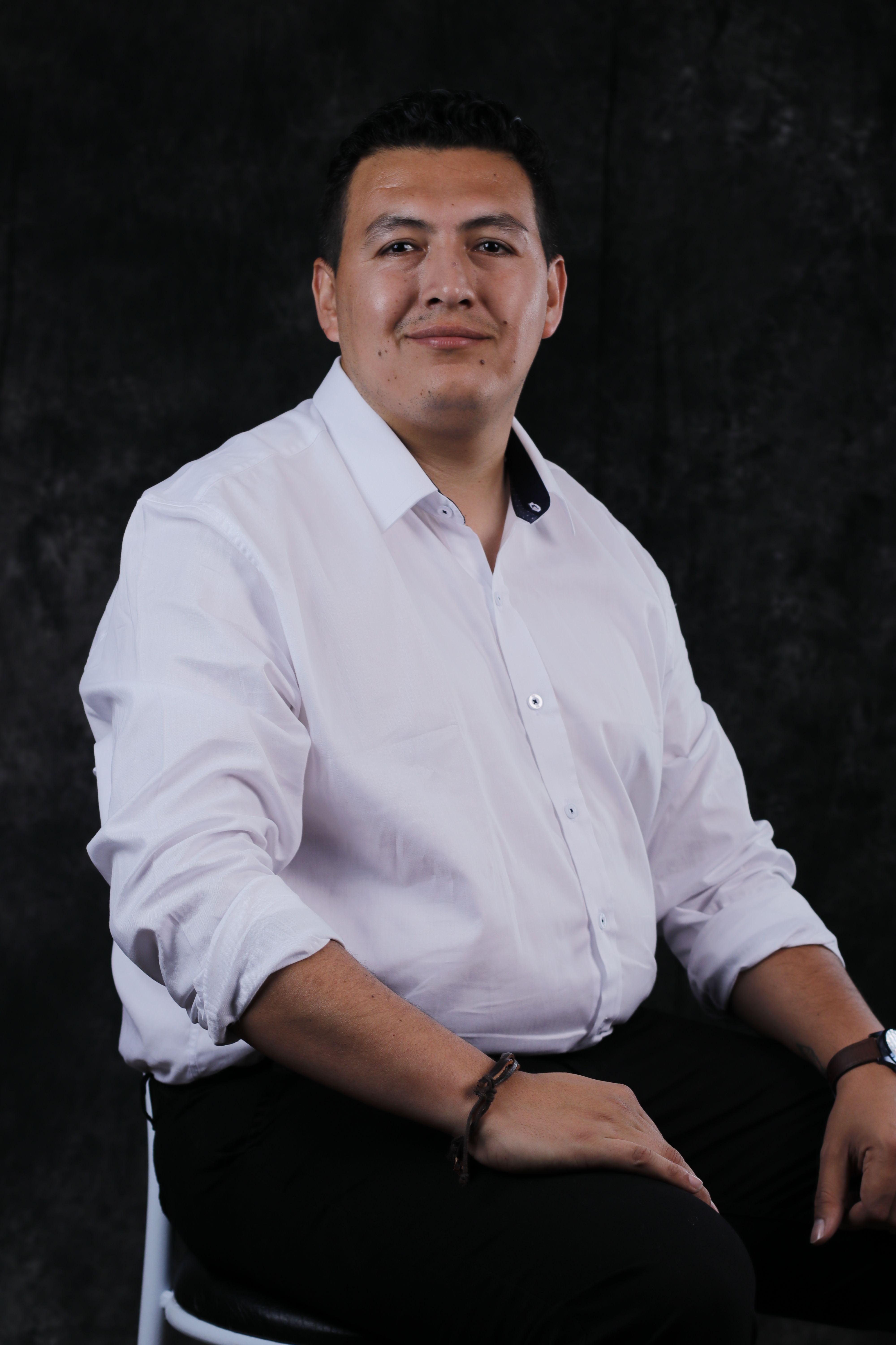 Studio portrait of a confident man seated with a neutral background, wearing a white shirt.
