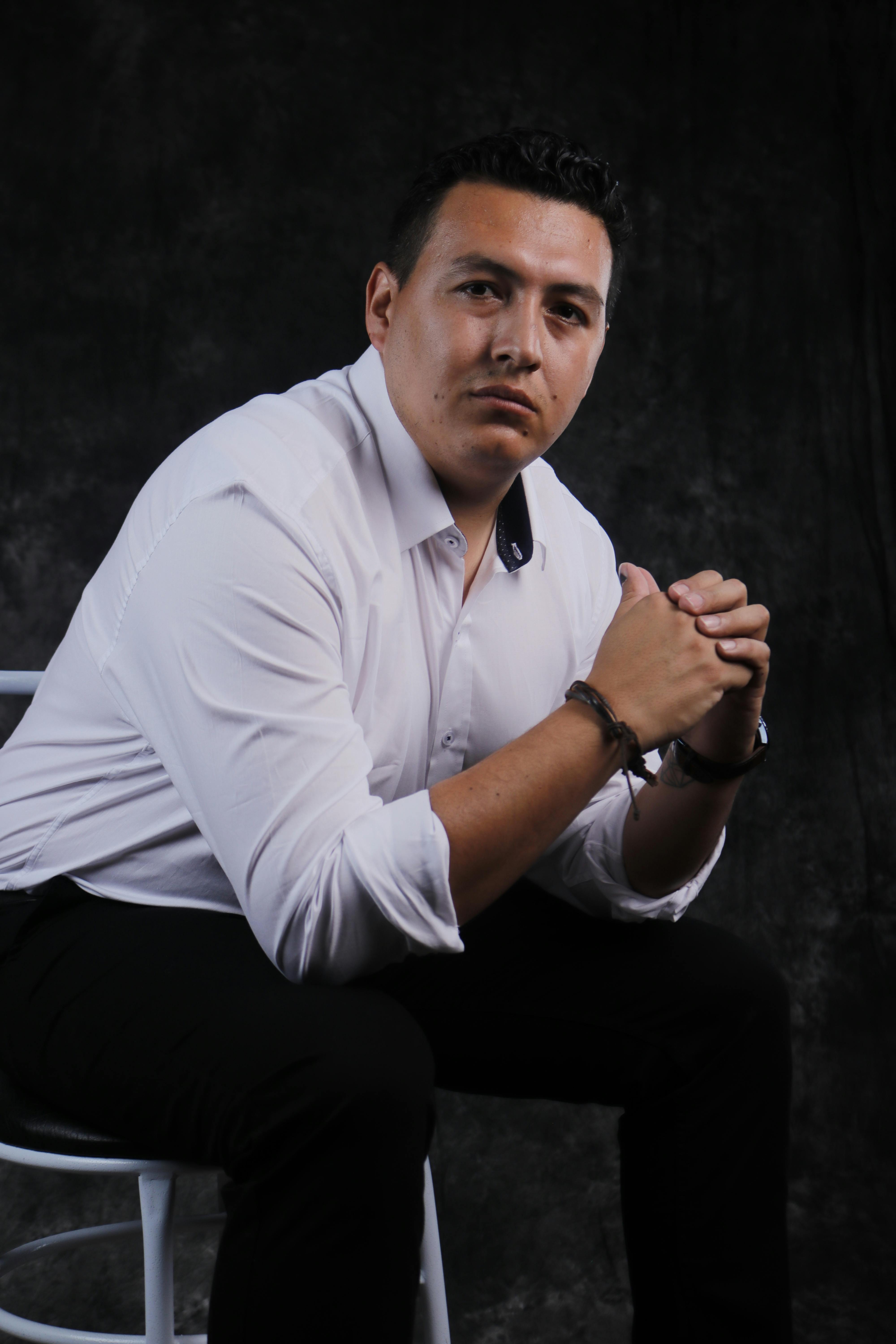 Portrait of a man in a white shirt seated, exuding confidence in a studio setting.