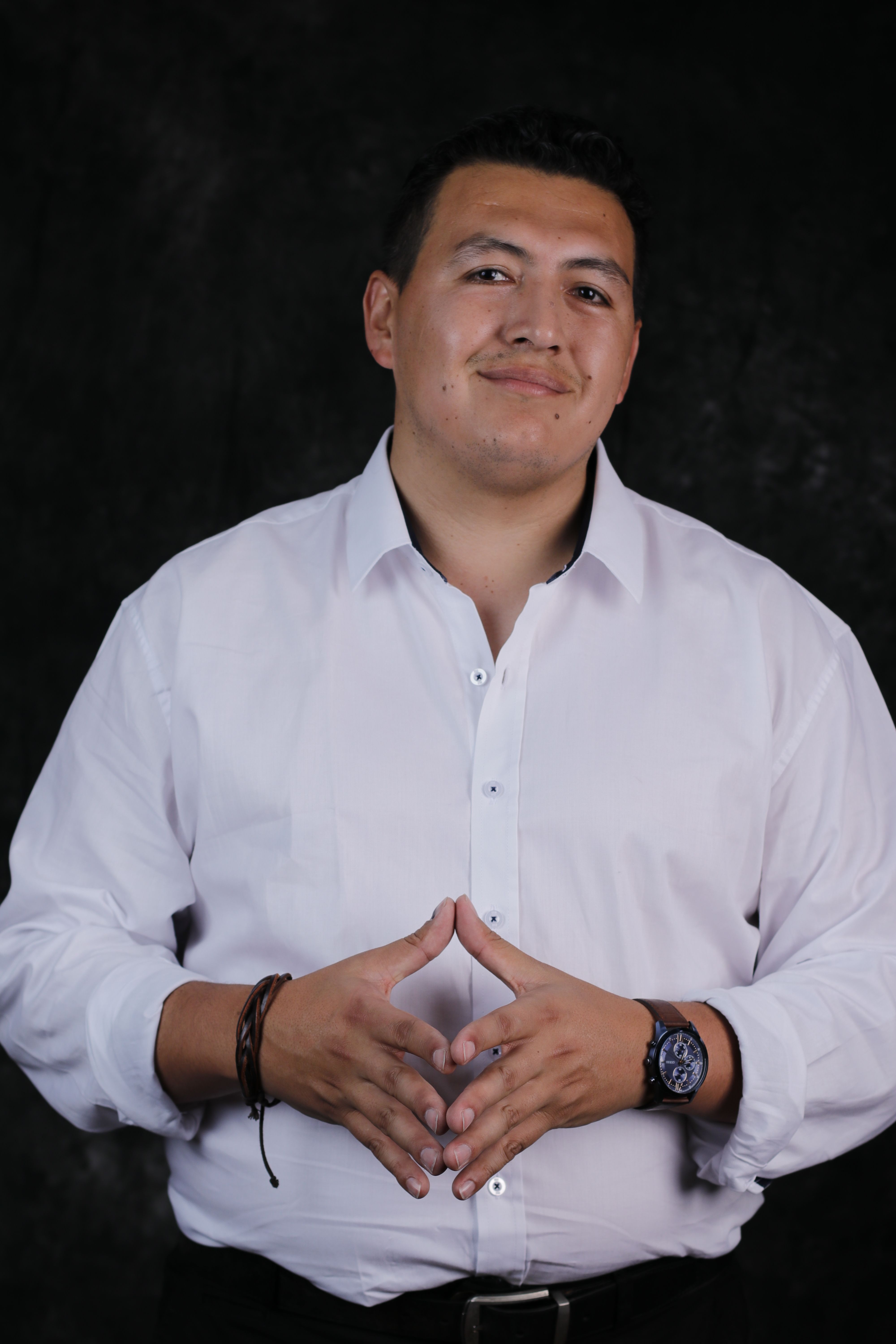 Portrait of a confident man in a white shirt posing against a dark background.