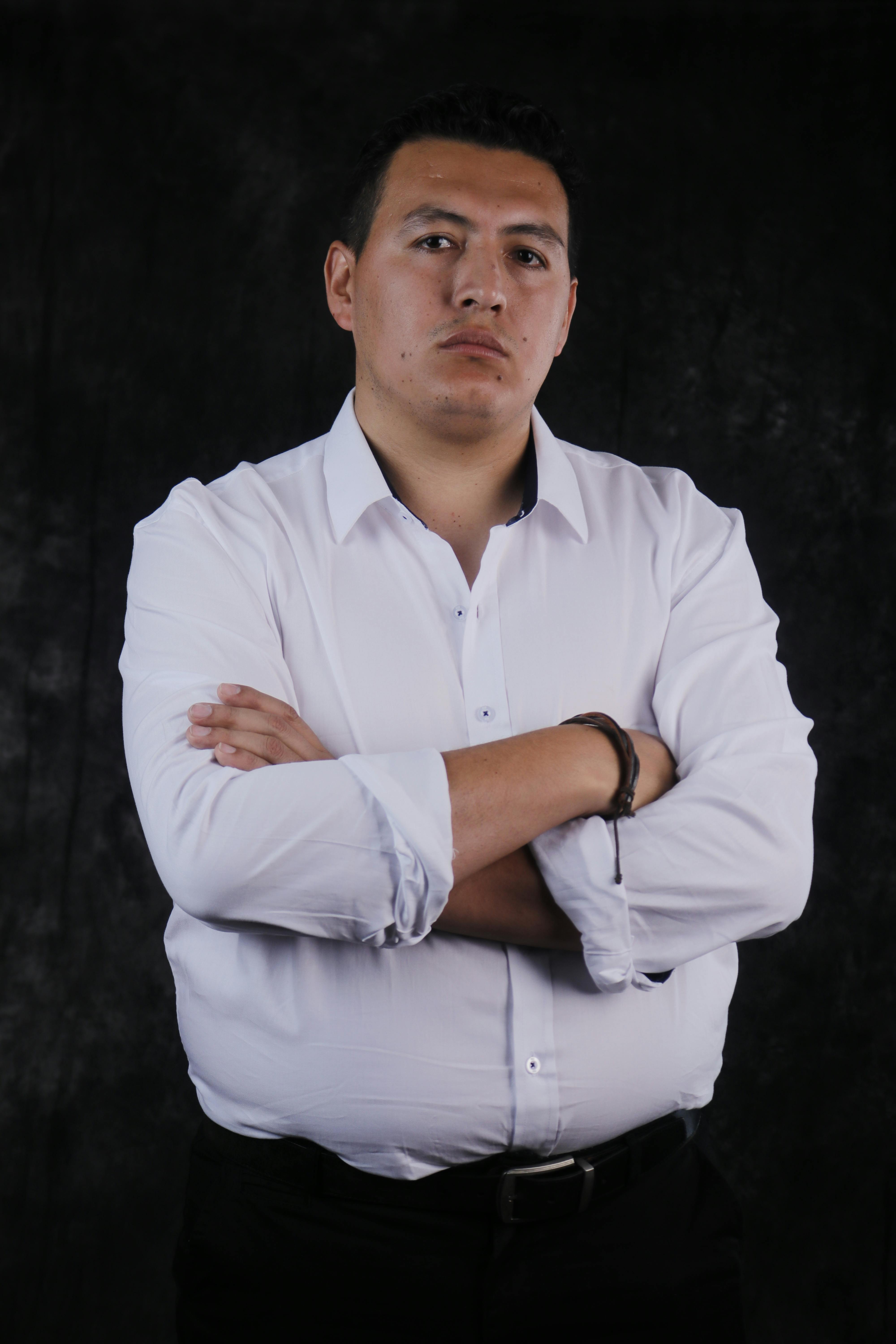Portrait of a confident young man in white shirt with arms crossed against a dark backdrop.