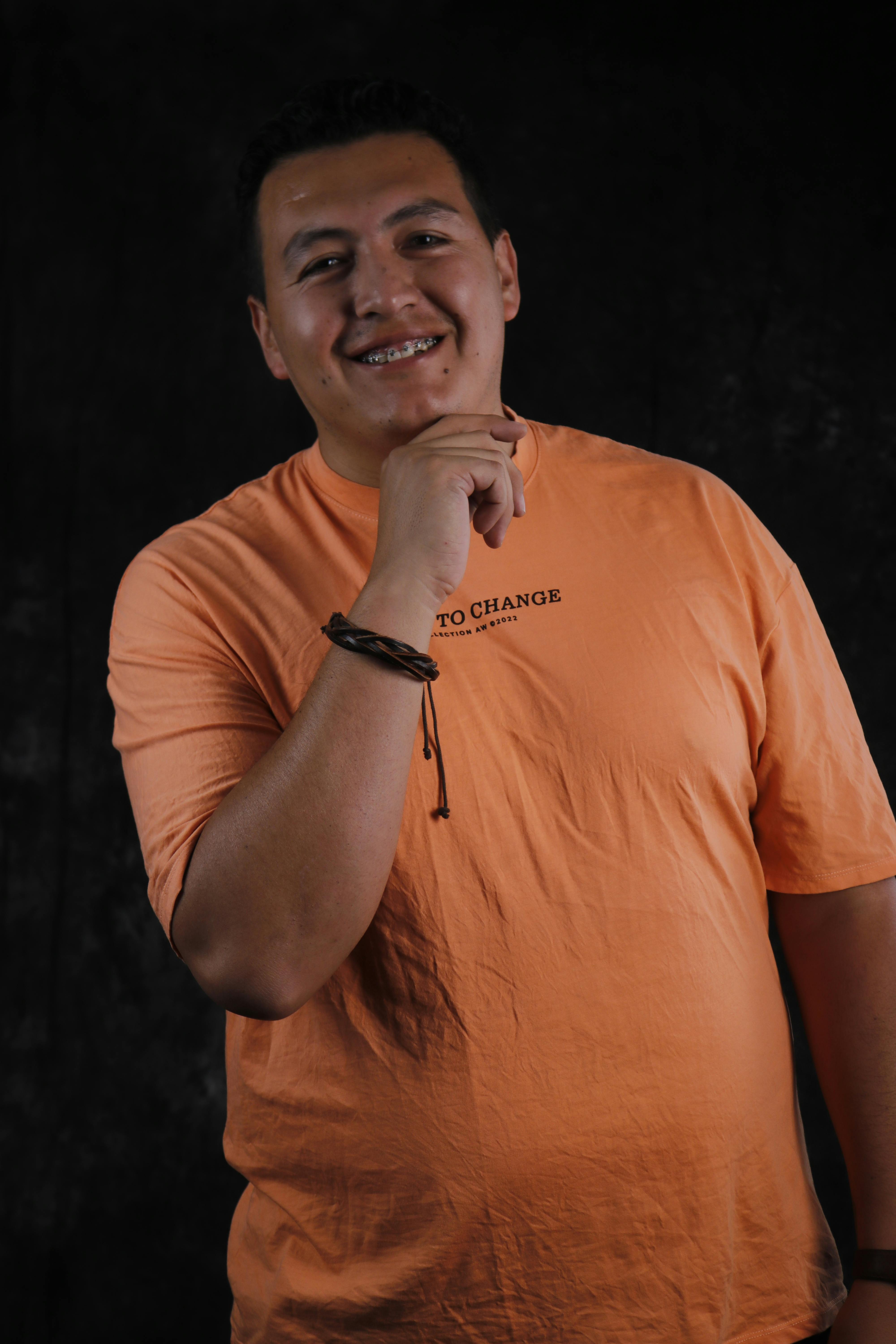 Portrait of a smiling man in an orange T-shirt posing against a dark backdrop.