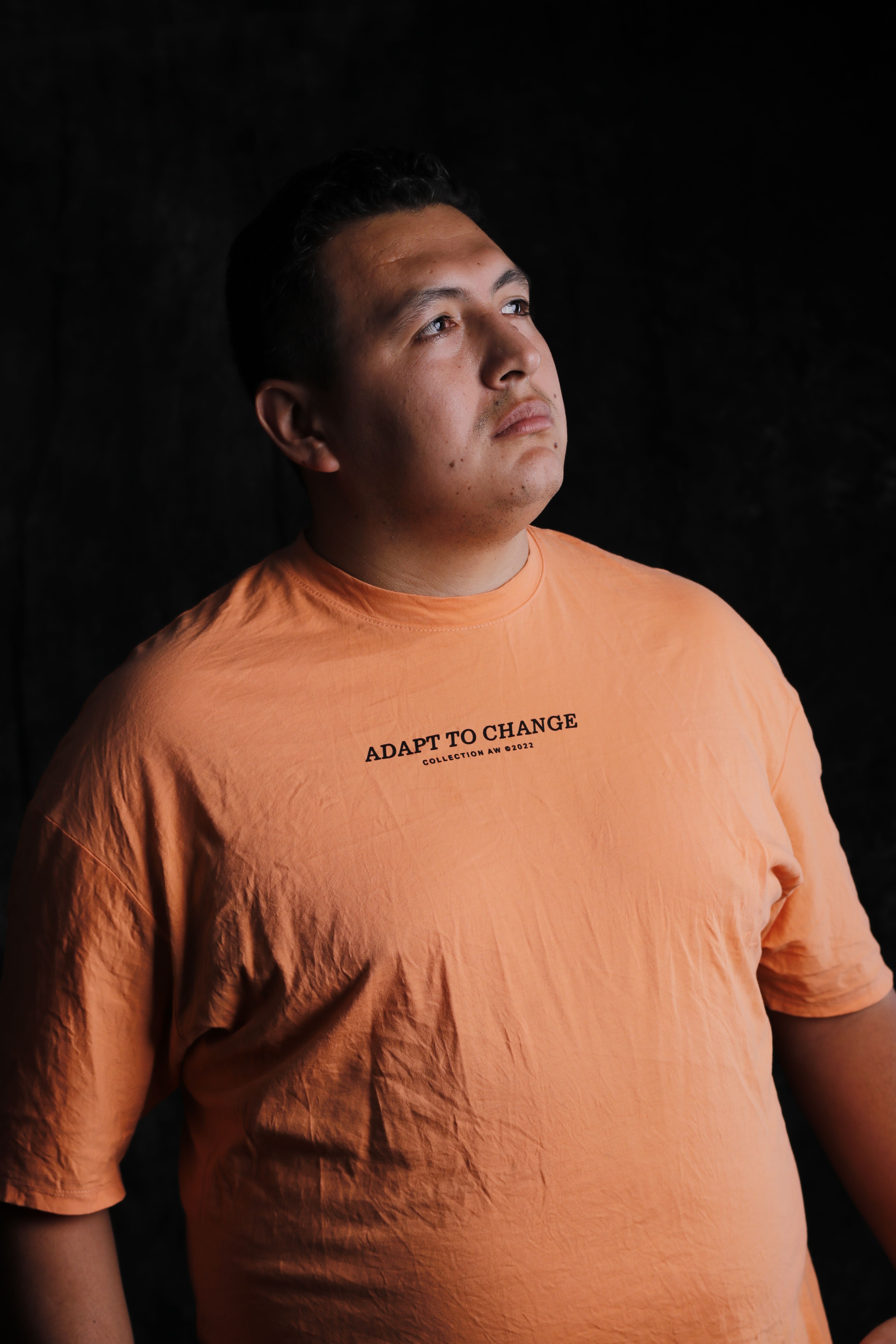 Contemplative portrait of a man in an orange T-shirt with a motivational message.