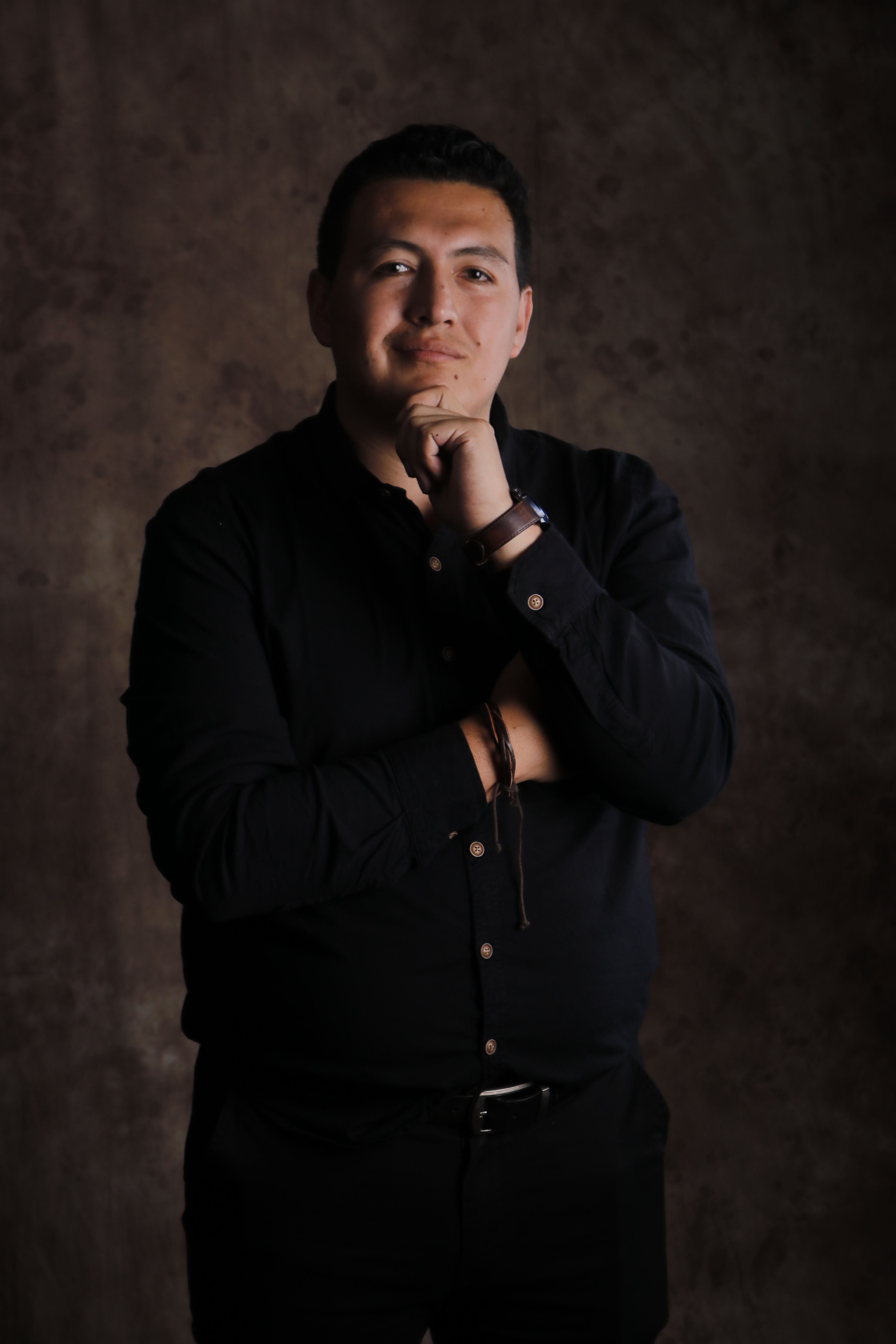 Portrait of a confident man standing in a studio with thoughtful expression and hand on chin.