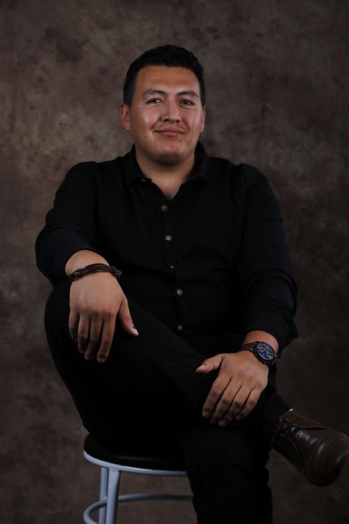 Free Portrait of a confident man sitting on a stool against a textured dark background. Stock Photo