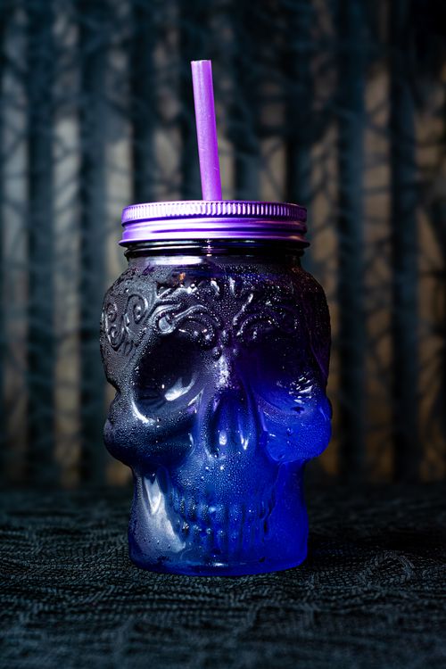 Free Dark-themed skull glass with a purple straw, perfect for Halloween or Día de Muertos celebrations. Stock Photo