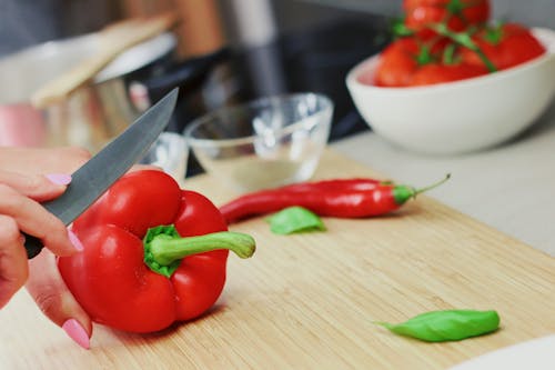 Person Slicing Red Chili Pepper on Brown Wooden Chopping Board