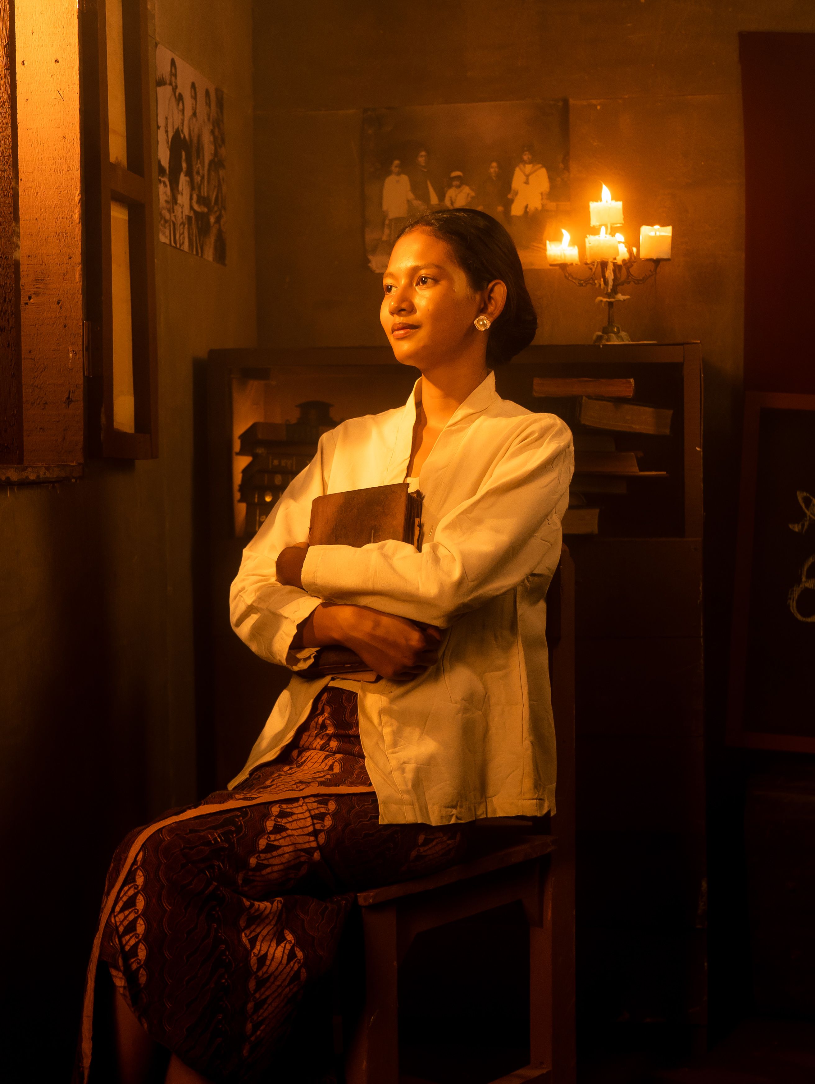A serene woman sits in a candlelit room holding a book, reflecting a warm and contemplative mood.