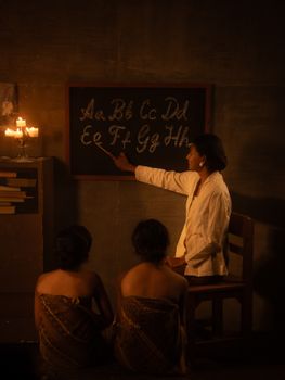 Teacher instructs students by candlelight in a traditional classroom setting.