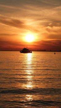 A tranquil sunset casting golden hues over the ocean with a ferry silhouetted against the horizon.