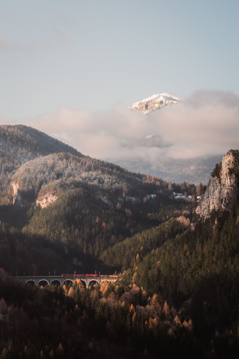Picturesque view of a train crossing the iconic bridge in Semmering Pass, Austria, with misty mountains.