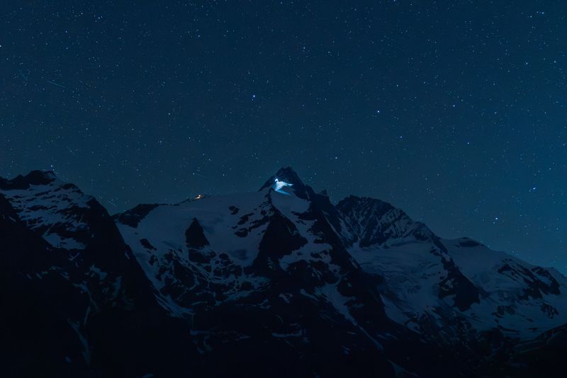 A breathtaking night sky above the majestic snowy peaks of Carinthia, Austria, featuring a starry expanse.