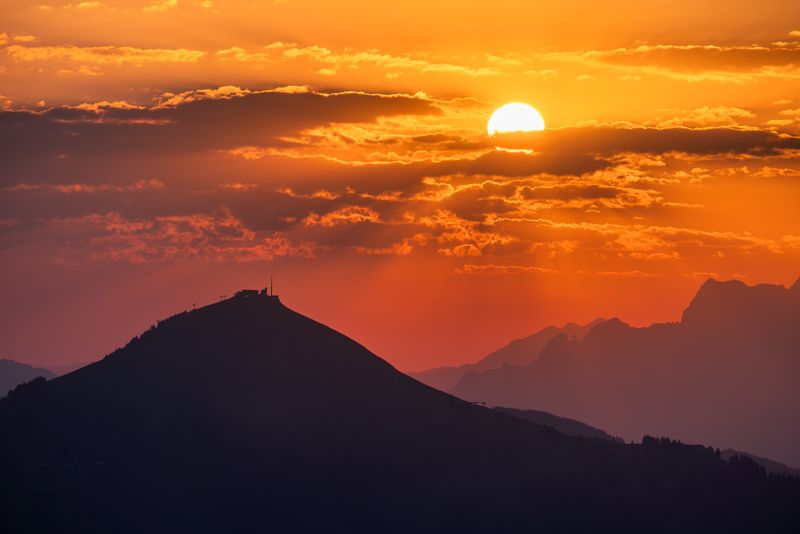 Stunning sunset over Tyrol, Austria with vibrant orange skies and mountain silhouette.