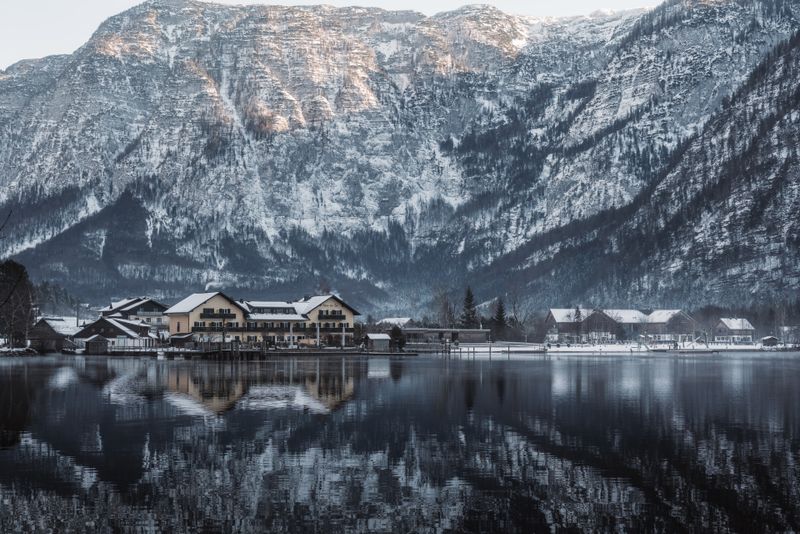Scenic winter view of Hallstatt with mountain reflections, snow-covered landscape, and calm lake.