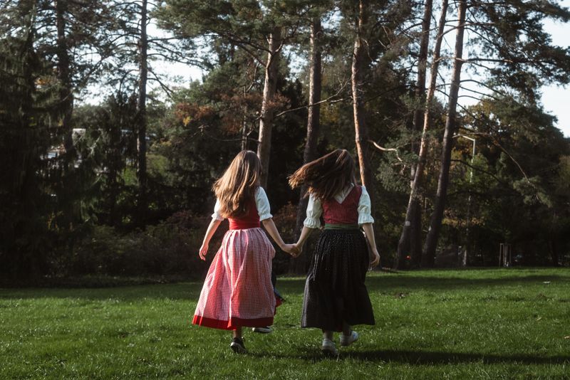 Two girls in traditional attire holding hands while walking in a lush green park on a sunny day.
