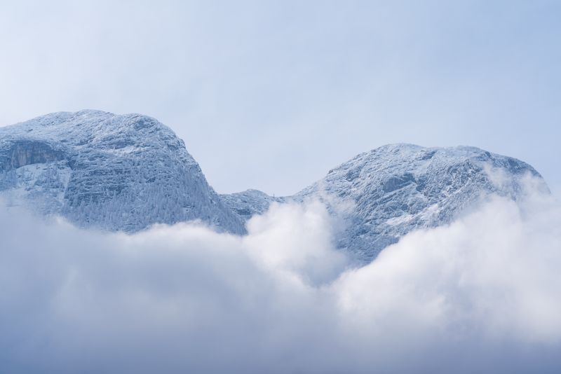 Experience the serene beauty of Hallstatt's snow-covered alpine peaks, framed by misty clouds.