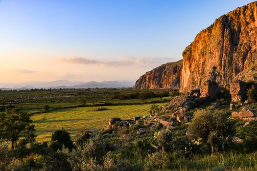 Beautiful sunset over ancient ruins and lush fields in Adana, Türkiye with rocky cliffs in the background.