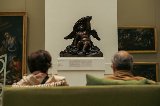 Two adults admire a classic sculpture in a Budapest museum filled with historic paintings.