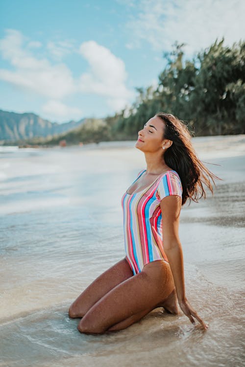 Free Woman in a Multicolored Swimsuit Sitting on Beach Stock Photo
