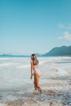 阳光明媚的日子里，一名身穿彩色泳衣的女子在海滩上享受着温暖的海浪