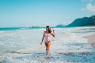 一名身穿彩色泳衣的女子，正走在沙滩上，背景是海浪和山脉