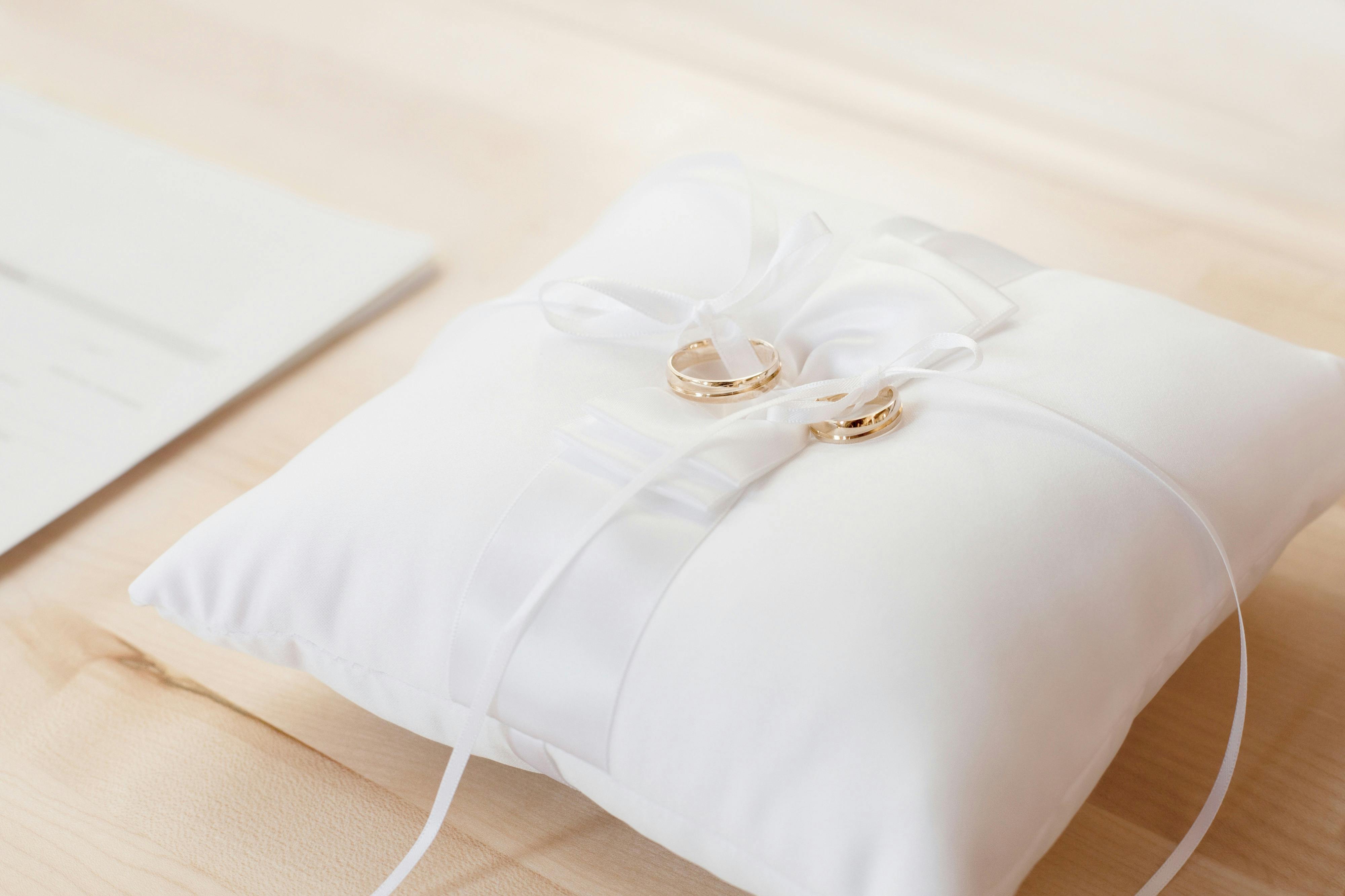 closeup photo of pair of gold bridal rings on top of white pillow