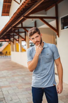 一位留着胡须的时尚男子身着休闲装，在城市背景下若有所思地摆出姿势