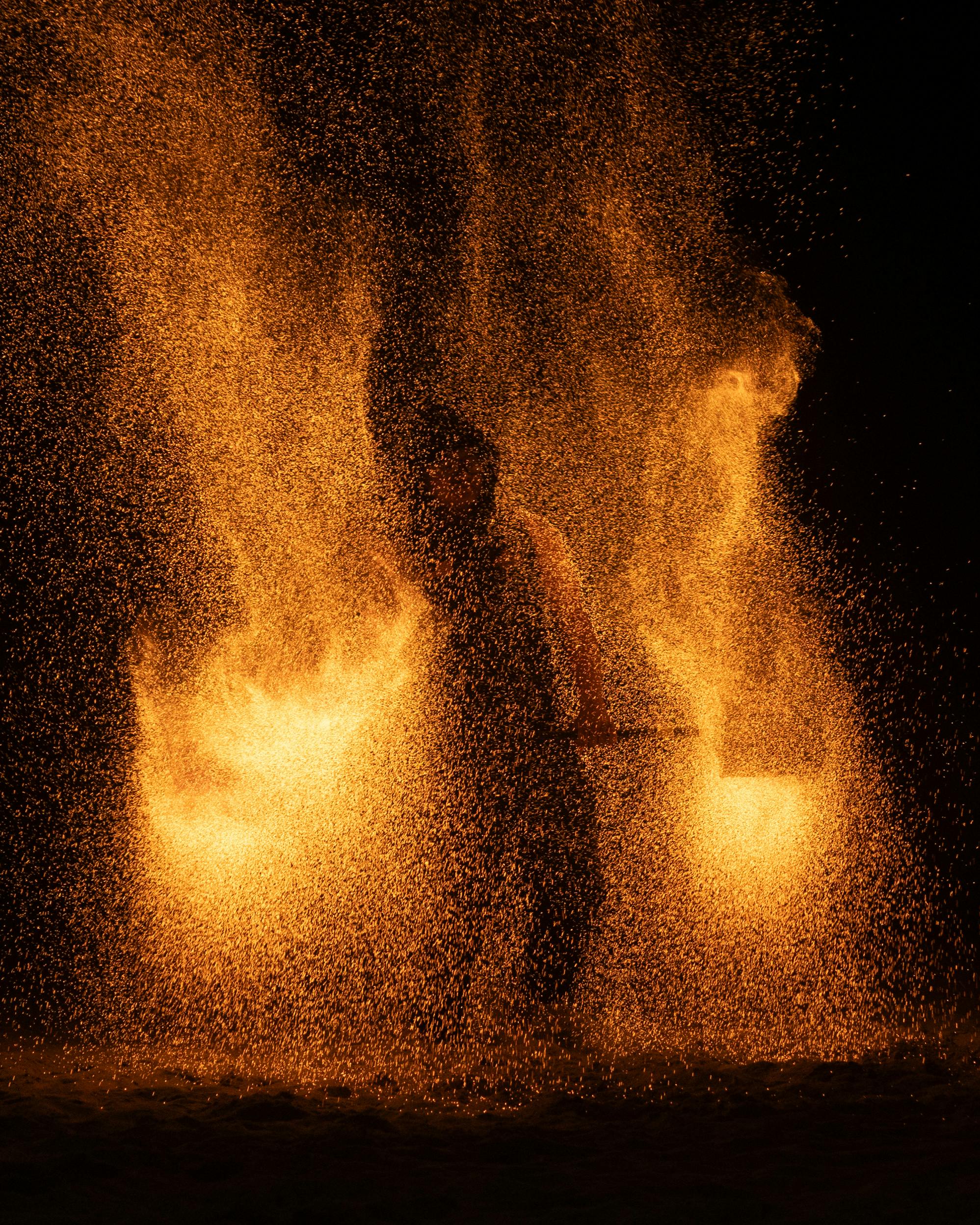 A captivating fire dance performance at night, illuminating the dark surroundings with fiery orange sparks.