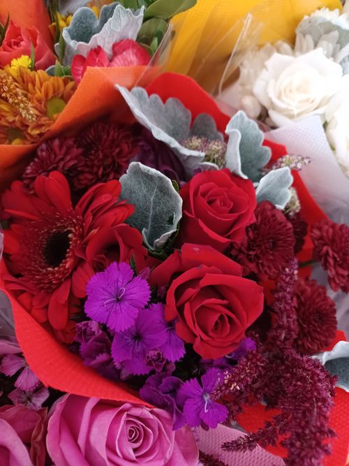 Free Colorful bouquet featuring red roses, Gerbera, and other blooms in bright shades, wrapped artistically. Stock Photo