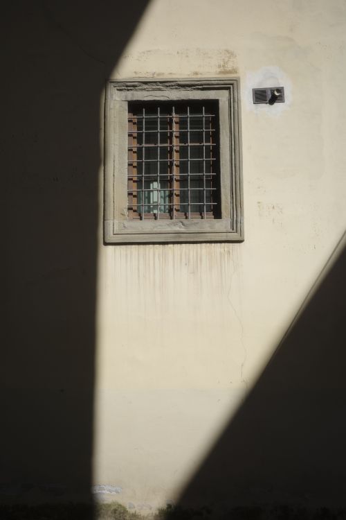 Free Artistic view of a grilled window against a textured wall with dramatic lighting and shadows. Stock Photo