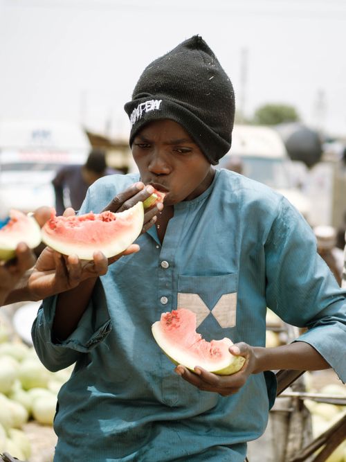 Free A boy in Zaria, Nigeria relishes fresh watermelon in an outdoor market setting. Stock Photo