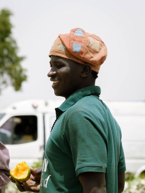 Free Cheerful man in Zaria, Nigeria, wearing cap and holding a mango outdoors. Stock Photo