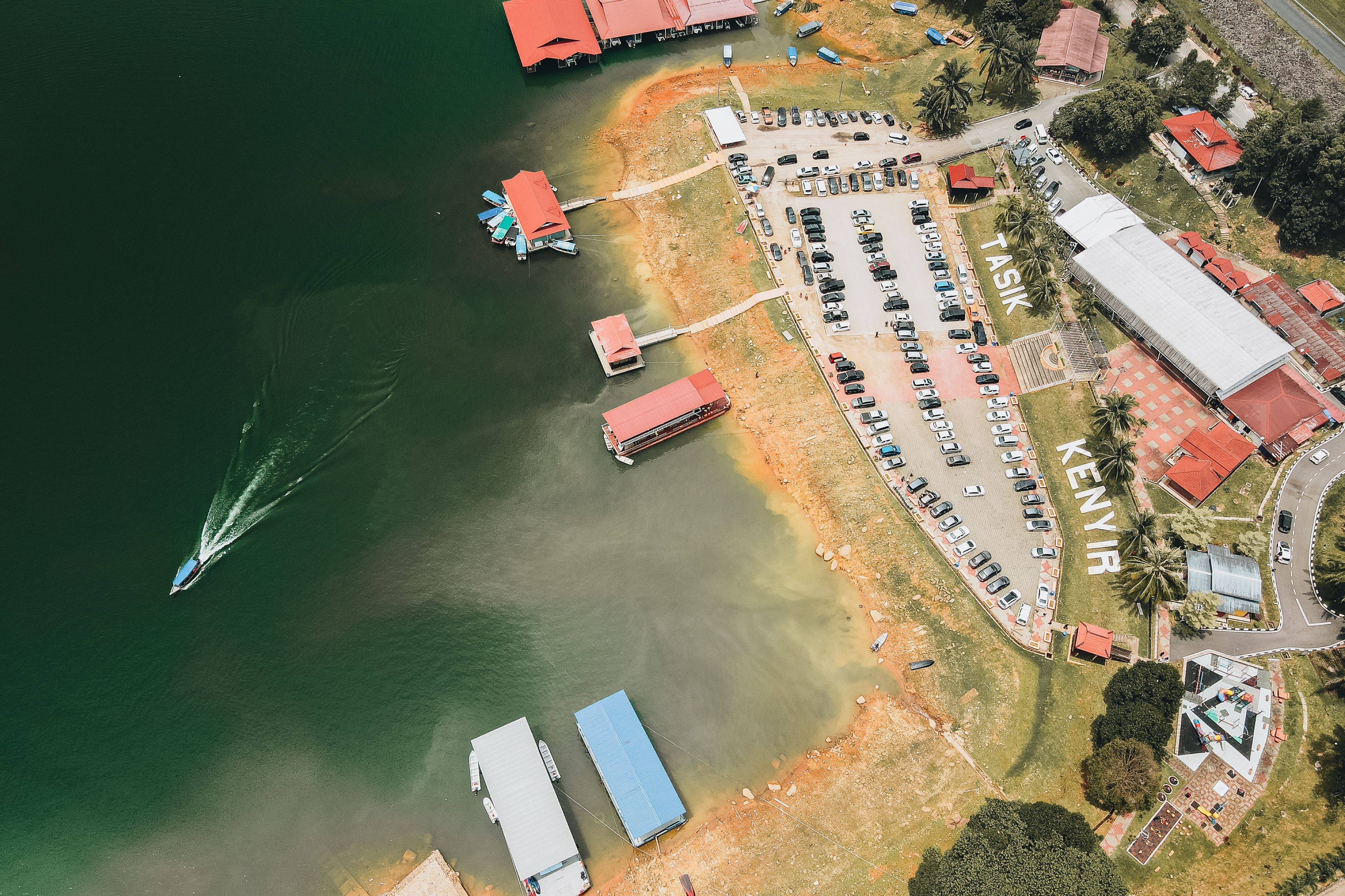 Aerial view of Tasik Kenyir, showcasing parked cars, buildings, and a boat on the lake.