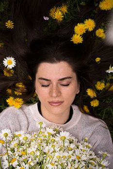 Woman lying among yellow and white daisies, eyes closed, relaxed expression, nature setting.