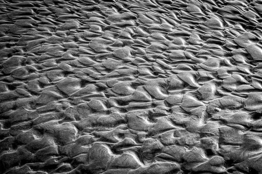 Close-up of textured sand patterns in black and white, resembling abstract art.